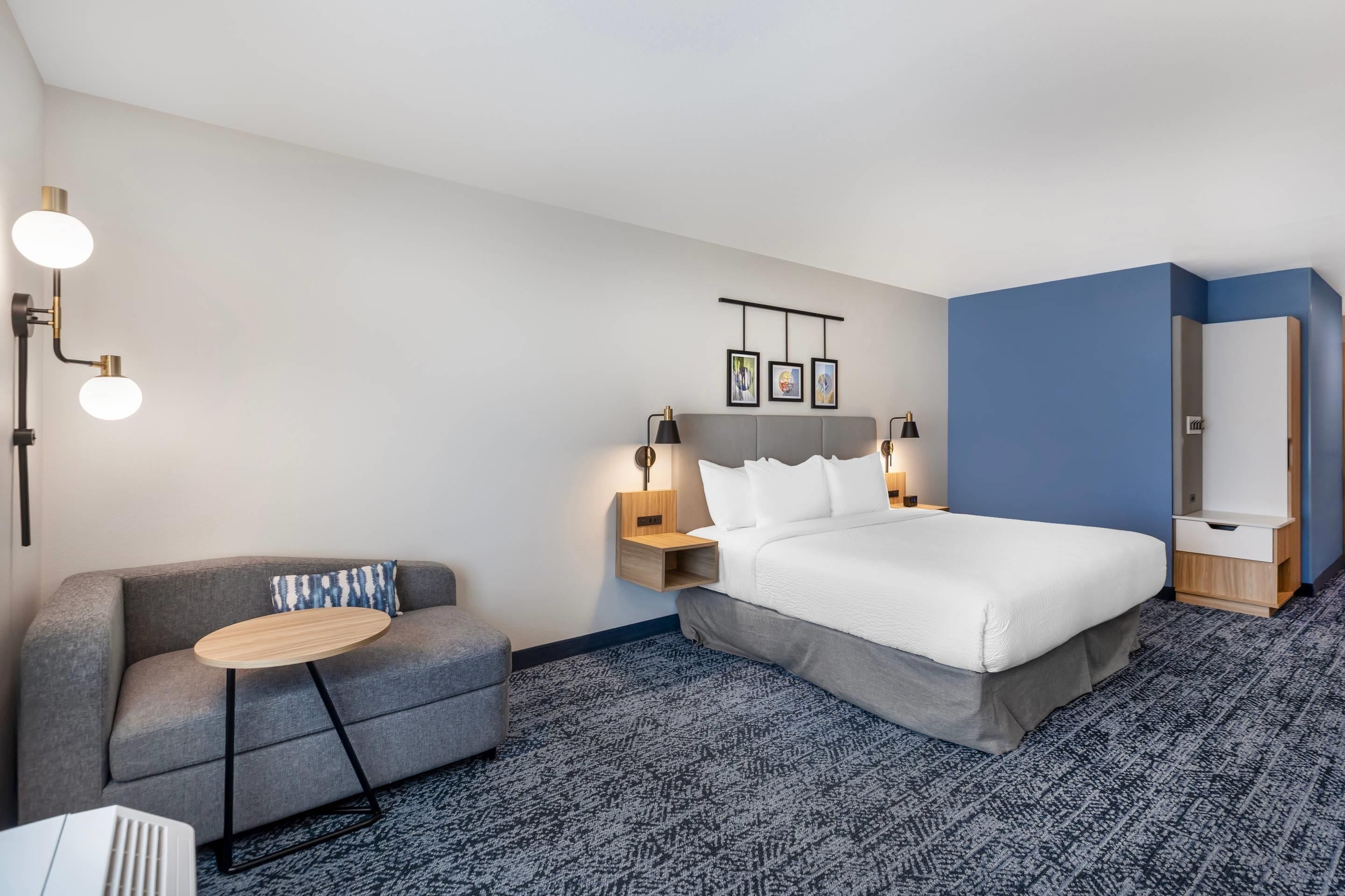 Une chambre d’hôtel avec un lit, un canapé, une petite table et une étagère fixée au mur.