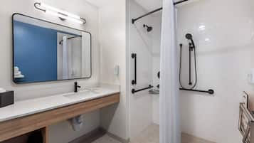 A modern bathroom with a large mirror, a shower with a handheld showerhead, and a toilet with a grab bar.