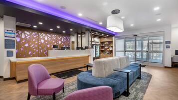 A hotel reception area with a modern design, featuring a reception desk, seating area with armchairs, and a large window providing a view.