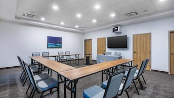 Una sala de conferencias con una larga mesa, sillas, un proyector y una televisión en la pared.