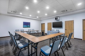 Ein Konferenzraum mit einem langen Tisch, Stühlen, einem Projektor und einem Fernseher an der Wand.