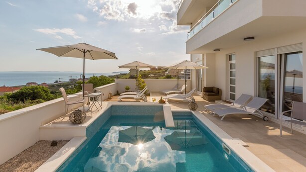 Piscina en la azotea con sillones de descanso y sombrillas, con vistas panorámicas al mar y edificios.