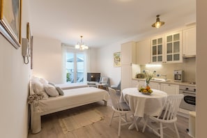 Una habitación de hotel compacta con cama, una mesa de comedor con sillas, kitchenette y un televisor pequeño.