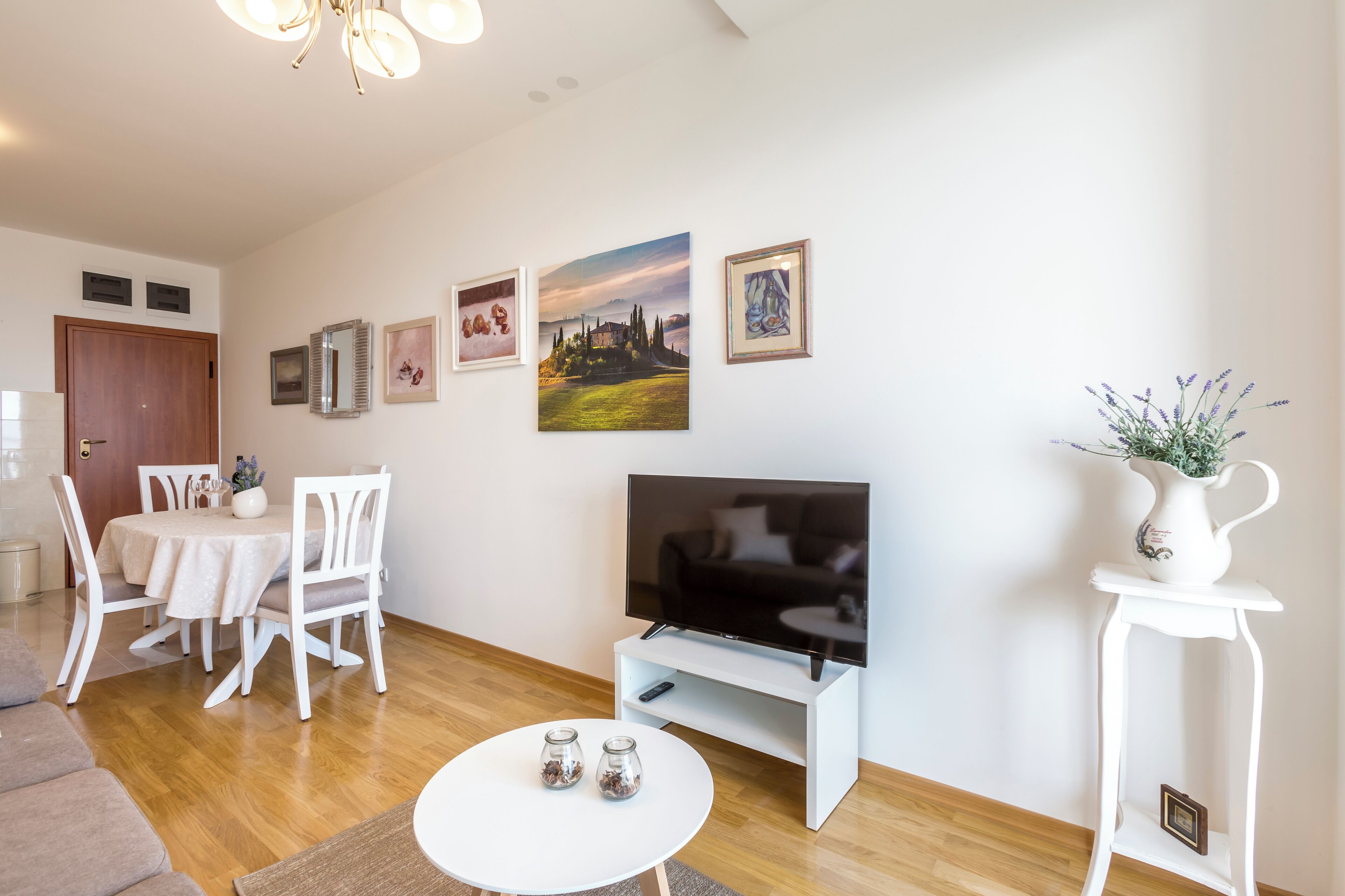 A modern living room with a dining area, a flat-screen TV, and artwork on the walls.