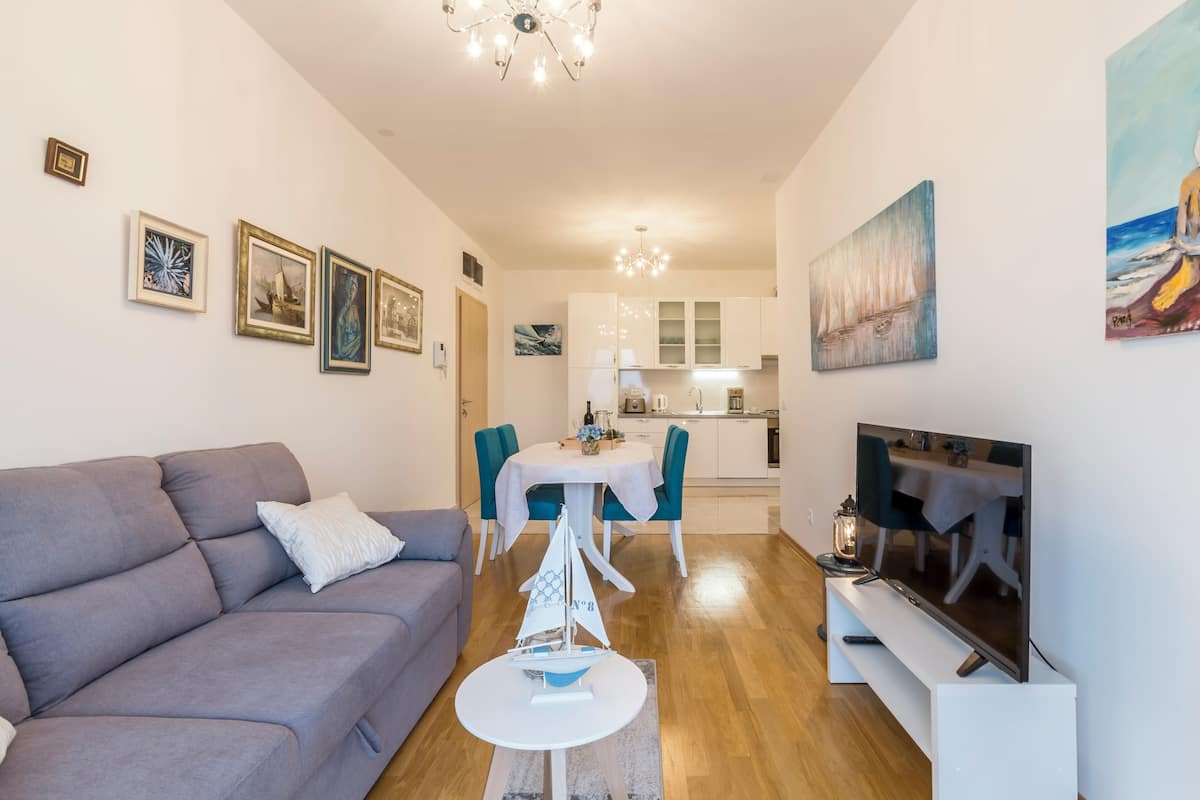 Una sala de estar moderna con un sofá gris, una mesita redonda con un barco modelo y un televisor de pantalla plana sobre un mueble.
