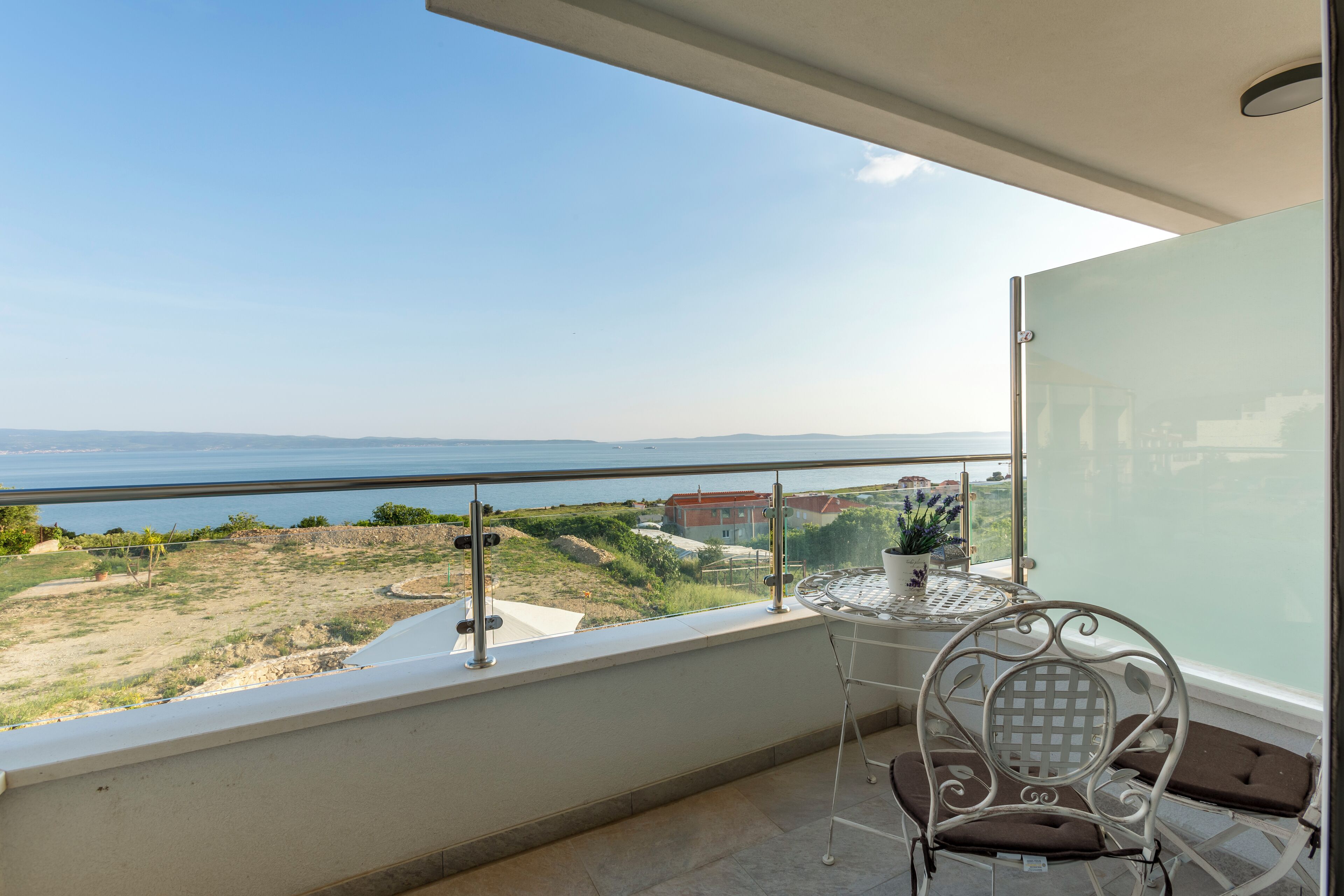 A balcony with a table and chairs, overlooking a coastal landscape with buildings in the distance.