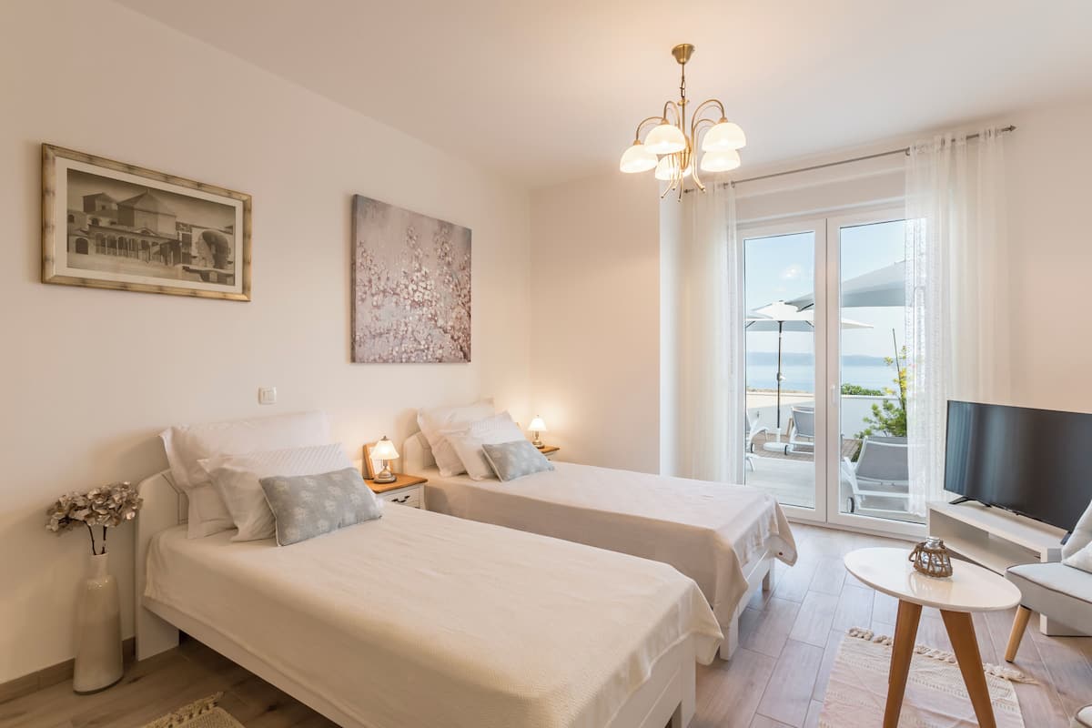 Habitación de hotel con dos camas, televisor, balcón con vistas y una araña.