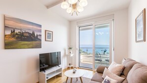 Una sala de estar moderna con televisor de pantalla plana, un sofá, una mesa de centro y un amplio ventanal con vistas al mar.