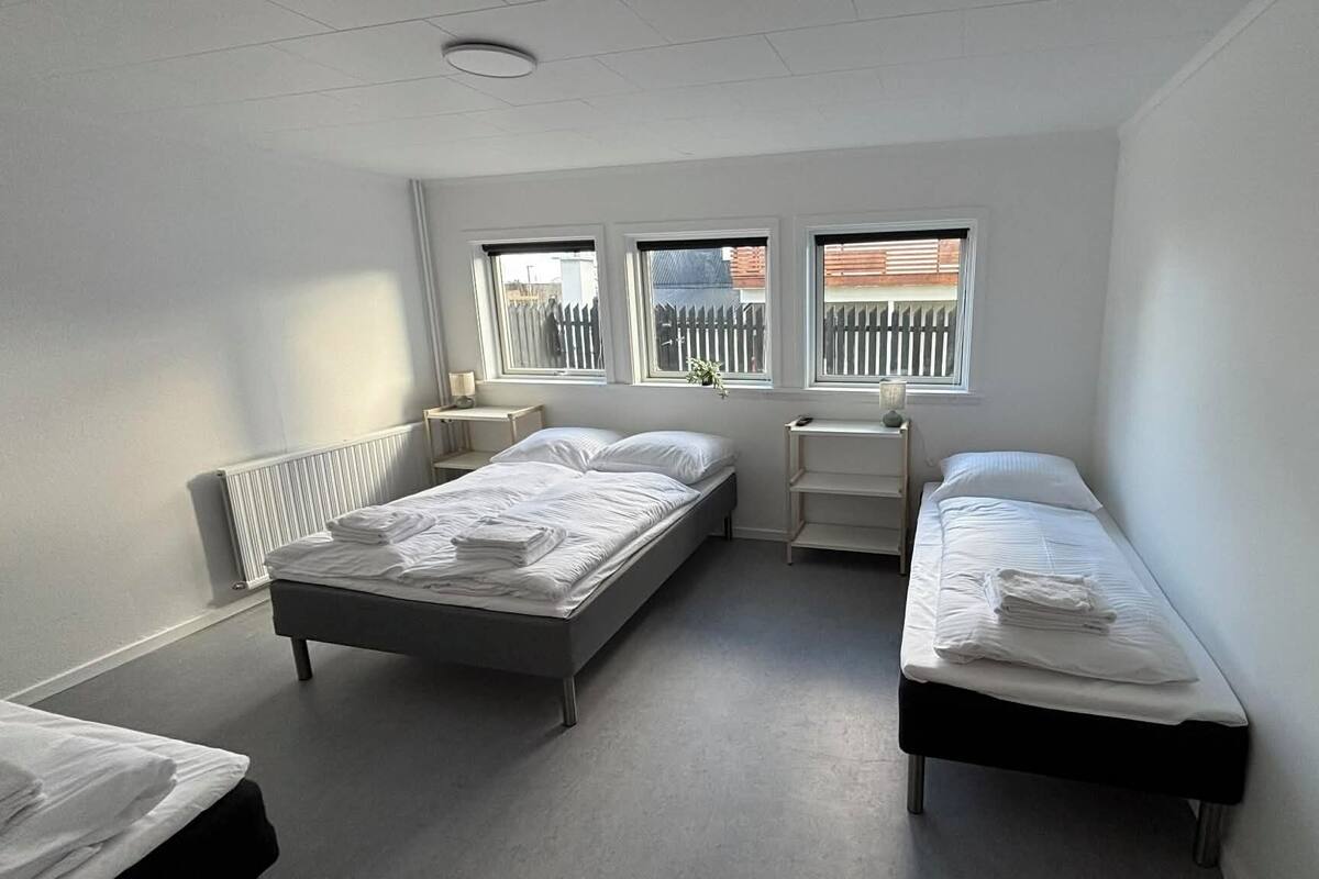 Une chambre avec deux lits, un radiateur, une fenêtre avec des stores et une table de chevet avec une lampe.