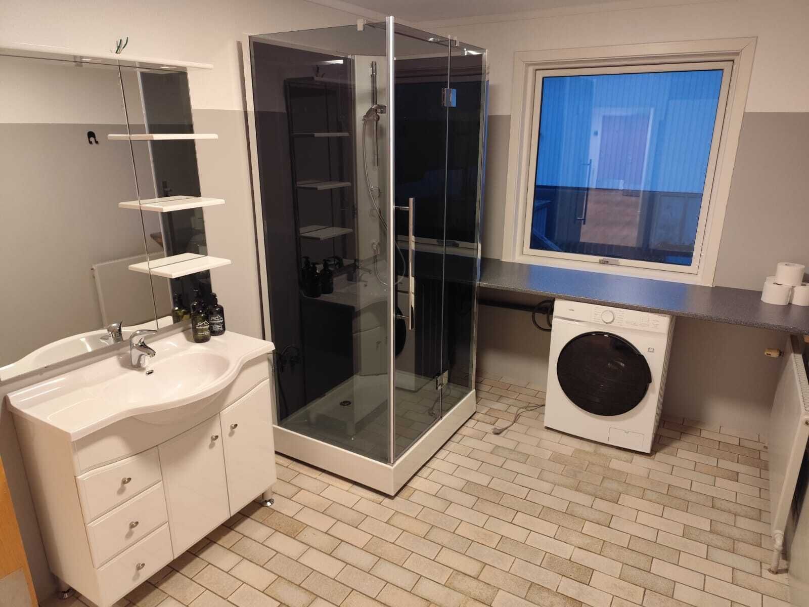 Un baño moderno con ducha de vidrio, lavamanos con espejo y lavadora.