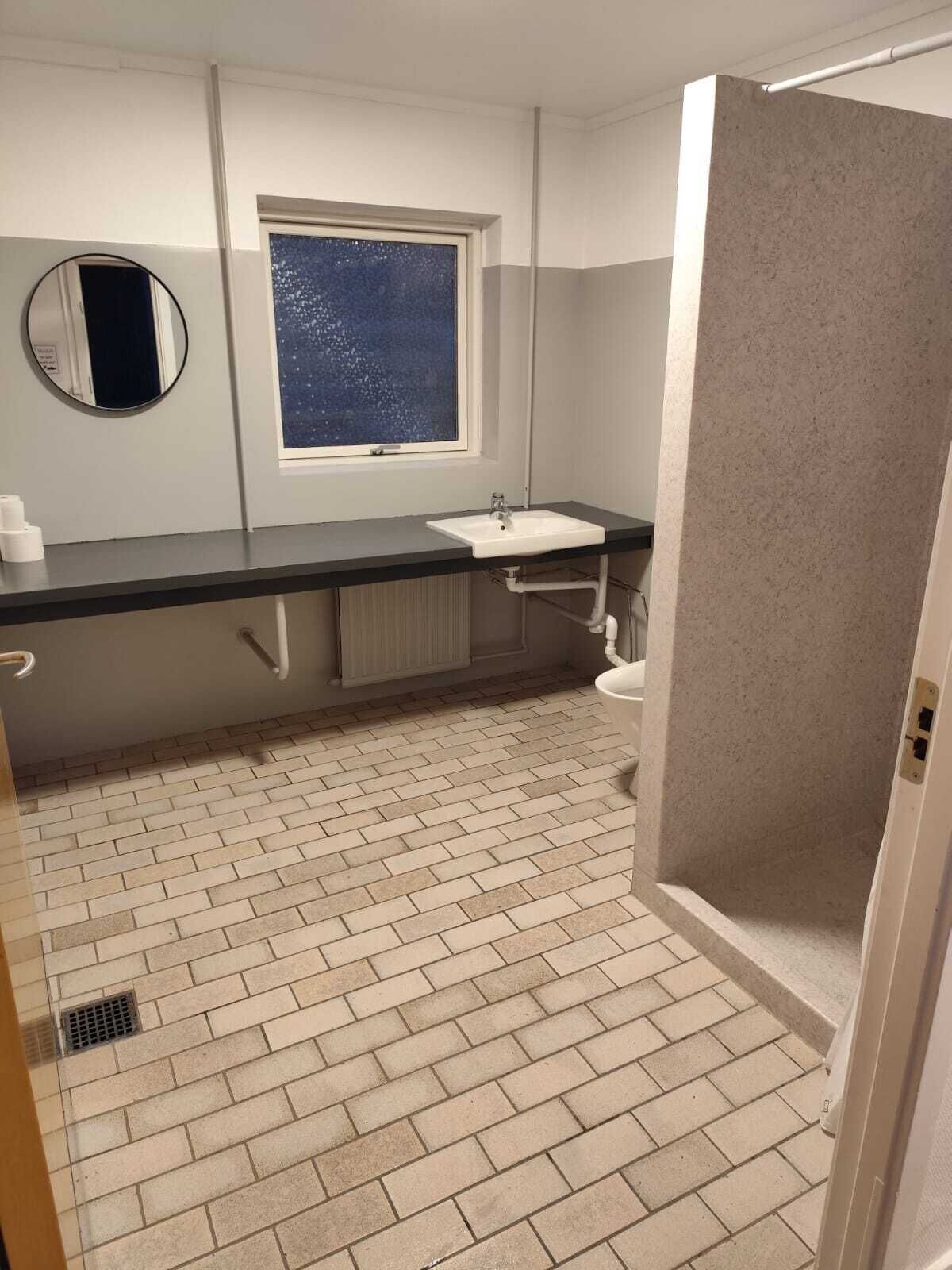 Un baño con lavamanos blanco, ventana con vistas, espejo y zona de ducha.