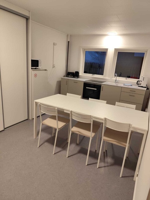 A compact kitchen with a white table and four chairs, a microwave, a coffee maker, and a window with a view of the outside. - Cozy Guest House in Tórshavn (Tórshavn)