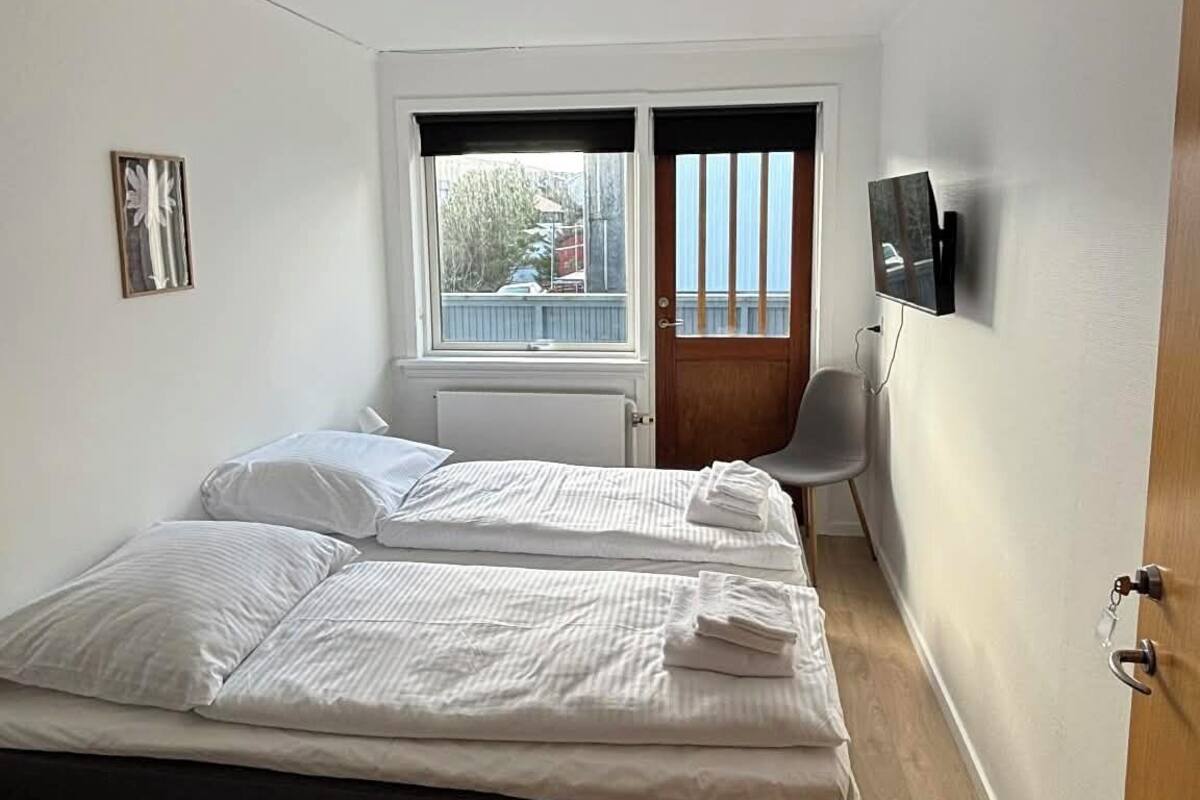 Une chambre à coucher avec un lit, une fenêtre, une chaise, un téléviseur et une porte.