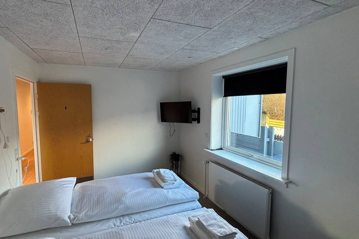 Une chambre à coucher avec un lit, un téléviseur fixé au mur, une fenêtre et une porte.