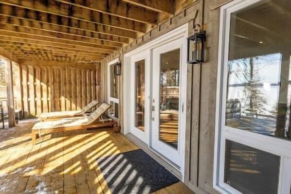 Un espace de détente en bois comprenant deux chaises longues et une porte vitrée donnant accès à une piscine.