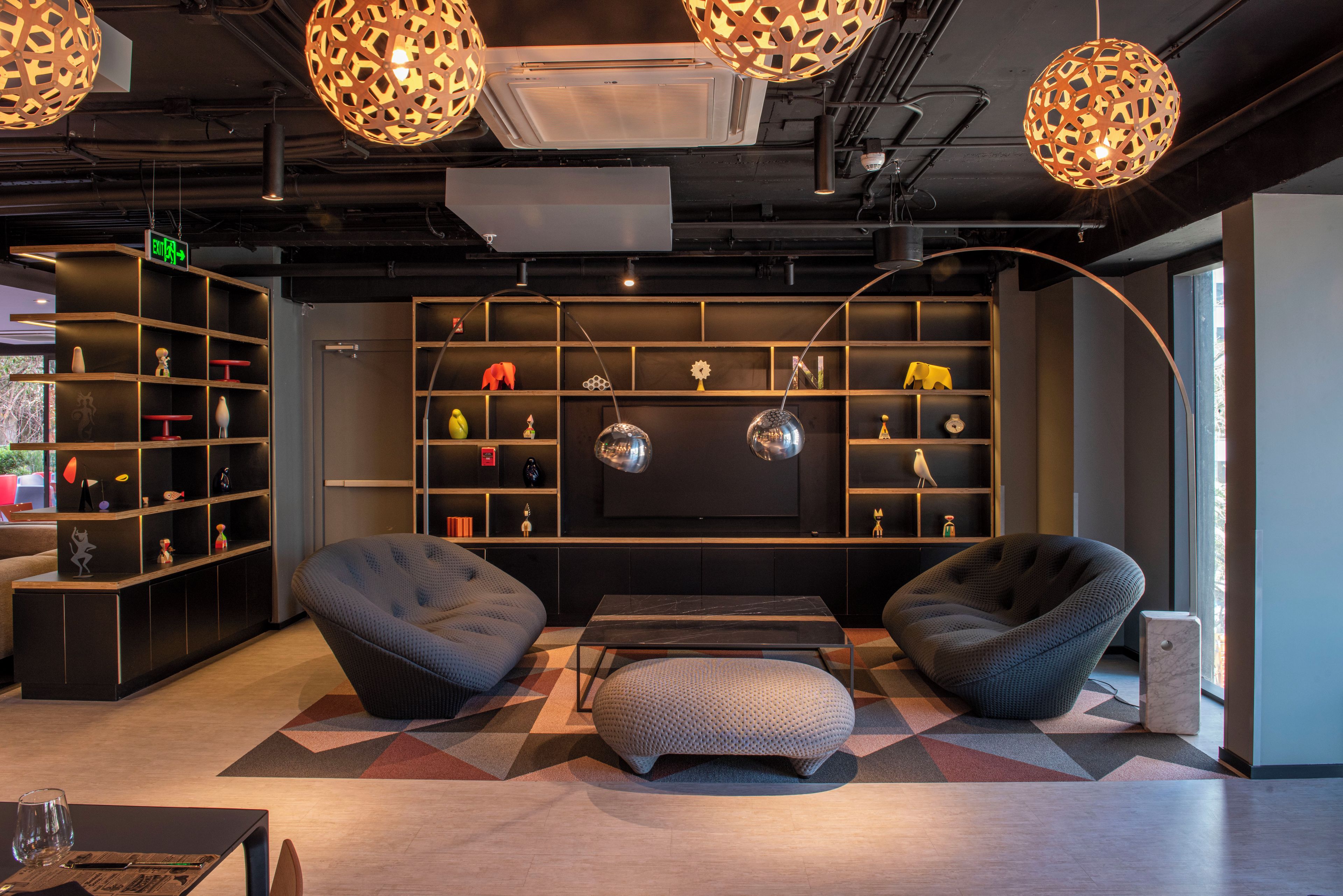 A modern lounge area with seating, shelves with decorative items, and a large window.
