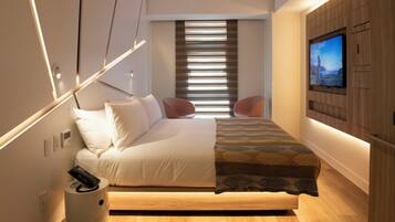 A modern bedroom with a bed, bedside table, TV, and a window with blinds.