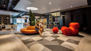 A modern interior with a seating area, a large plant, and a unique red chair. - Hotel Nodo (Santiago)