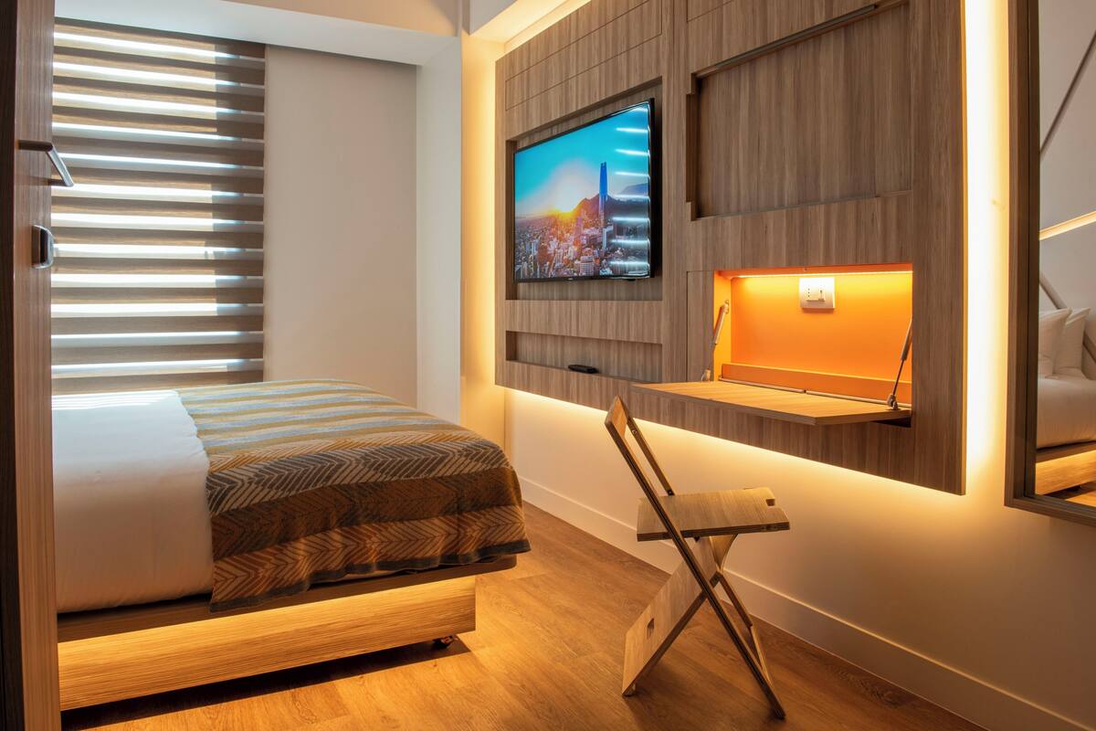 Habitació d'hotel moderna amb un llit, un televisor penjat a la paret i una zona de treball amb una cadira.