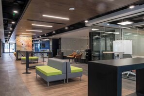 A modern office space with a long corridor, seating areas, glass partitions, and a whiteboard. - Hotel Nodo (Santiago)