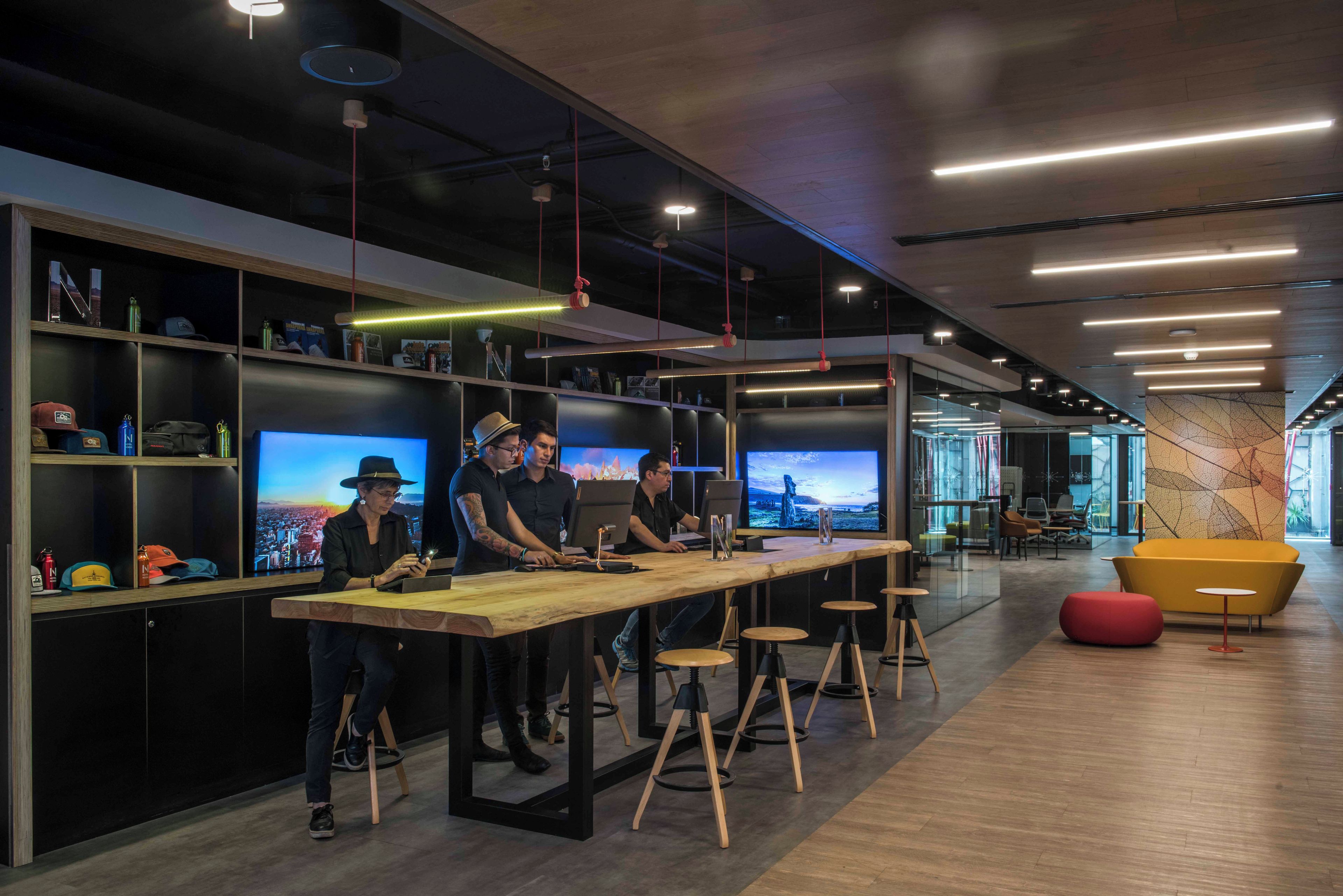 Um espaço de trabalho moderno com uma mesa comprida, várias telas e uma área de estar com uma cadeira amarela.