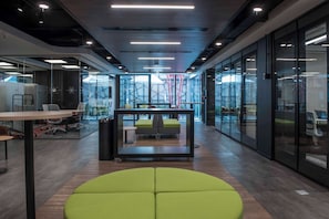 An office space with glass walls, a central seating area, and a modern ceiling design. - Hotel Nodo (Santiago)