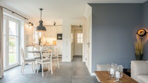 Een moderne keuken met witte kasten, een eethoek met een houten tafel en stoelen, en een zithoek met een bank en salontafel.