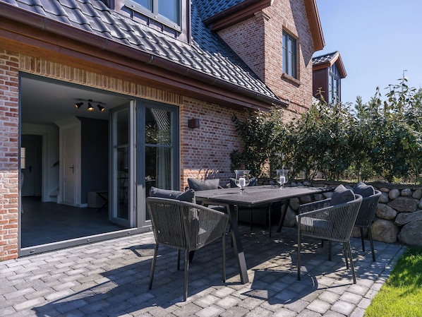 A patio with a table and chairs, a brick wall, and a glass door leading to an interior space.