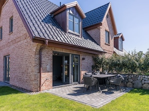 A brick house with a sloped roof, a patio with outdoor furniture, and a stone wall.