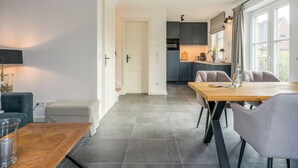Una cucina moderna con mobili grigi, un'area pranzo con tavolo e sedie di legno grigio, e vista all'esterno attraverso ampie finestre.