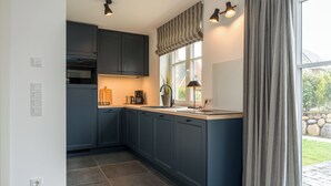 Una cucina moderna con pensili scuri blu, forno integrato, macchina del caffè e una finestra con tende.