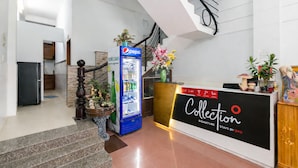 Ein Hotel-Empfangsbereich mit einem Pepsi-Kühlschrank, einem Empfangstresen mit der Aufschrift 'Collection Signature Stays by OYO' und einer Treppe.