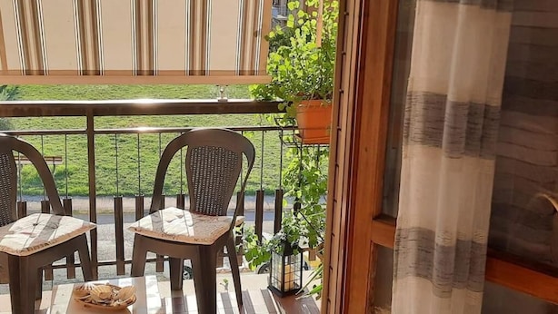 Ein Balkon mit zwei Stühlen, einem Tisch, einem Blumentopf und Blick auf eine grüne Landschaft.