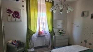 Ein Schlafzimmer mit Bett, Stuhl, Schminktisch und einem Fenster mit Vorhängen.