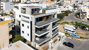 Un edificio moderno de varios pisos con balcones, una terraza en la azotea y un área de estacionamiento.