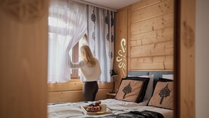 Un dormitorio con cama, almohadas, mesita de noche y ventana con cortinas.