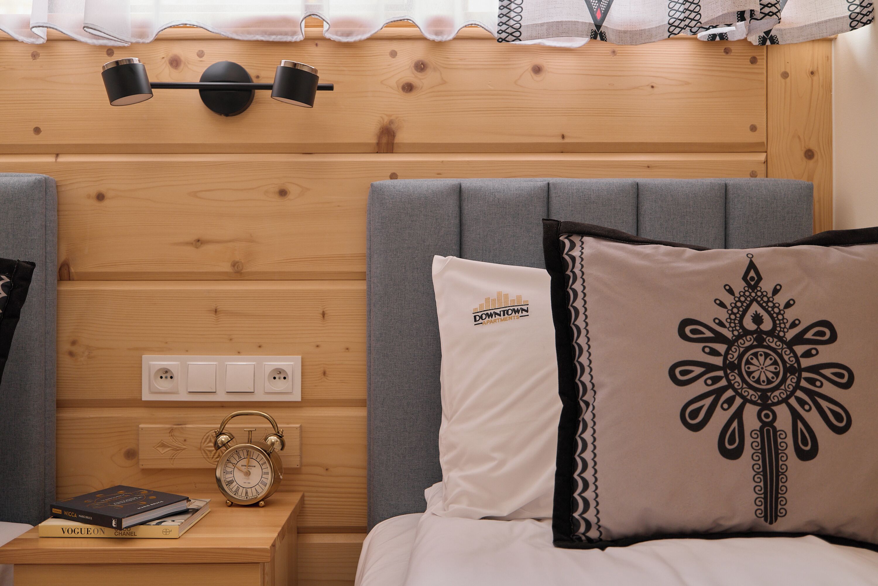 Ein Hotelzimmer mit einem Holzkopfteil, Nachttischlampen, einer Uhr und einem Bett mit gemusterten Kissen.