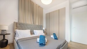 Ein modernes Hotelzimmer mit einem großen Bett, einem Nachttisch, einer Lampe und einem Kleiderschrank.