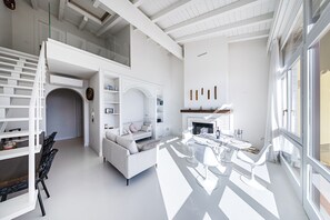 Ein geräumiger Wohnbereich mit einer Couch, einem Esstisch, Stühlen, einem Kamin und einer Treppe zu einer oberen Ebene.