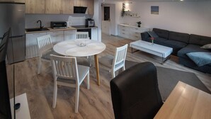 Una cocina moderna con electrodomésticos de acero inoxidable, un comedor con una mesa redonda y sillas, y una sala de estar con sofá y una mesa de centro.
