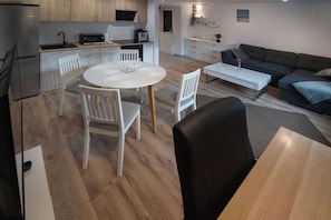 A modern kitchen with stainless steel appliances, a dining area with a round table and chairs, and a living area with a sofa and coffee table.