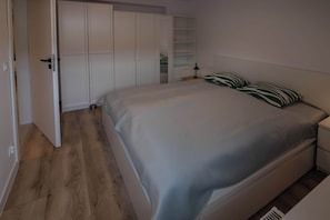 A bedroom with a bed, a nightstand, a lamp, and a wardrobe.