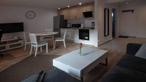 Una sala de estar moderna con una mesa de centro blanca, sofás grises y un comedor con sillas blancas.