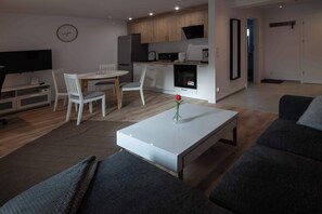 A modern living room with a white coffee table, grey sofas, and a dining area with white chairs.