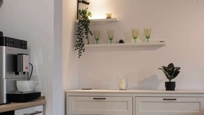Una cocina moderna con cafetera, armarios blancos y estantes decorativos.