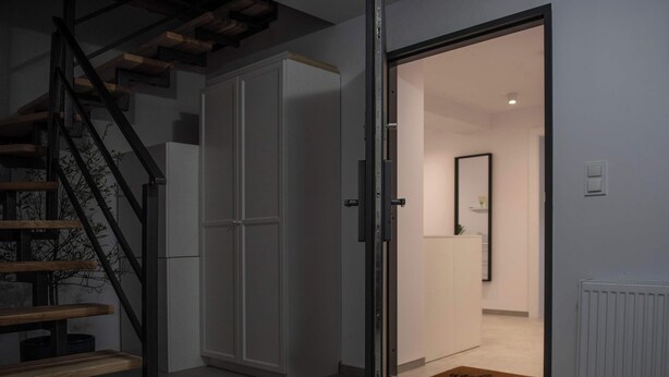 Un interior moderno con una escalera de madera, un armario y una puerta que da a una habitación con un espejo y un radiador.