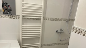 Um banheiro com pia branca, porta-toalhas, chuveiro com barra para segurar e piso de azulejo com padrão quadriculado.