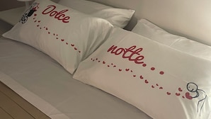 Uma cama com duas almofadas exibindo a inscrição 'Dolce notte' e um pequeno desenho de uma pessoa mandando um beijo.