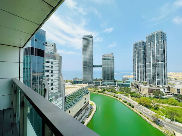 A modern high-rise building with a glass facade overlooking a green waterfront.