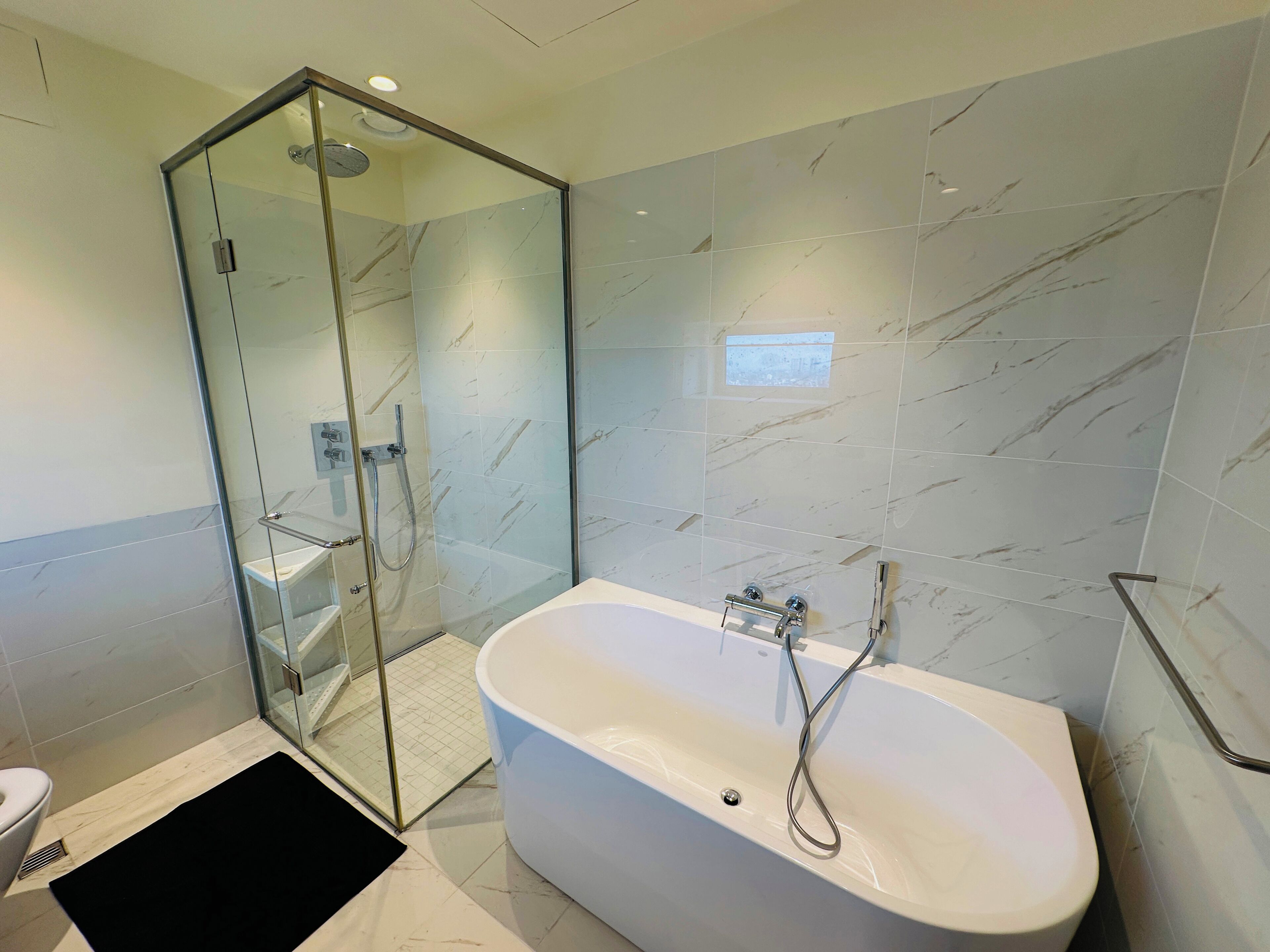 Ein modernes Badezimmer mit einer begehbaren Glasdusche, einer freistehenden Badewanne und Marmorfliesen.